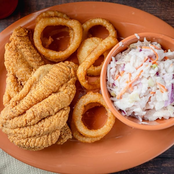 Soul Goode's fried catfish, crispy onion rings, and creamy coleslaw on an orange plate.