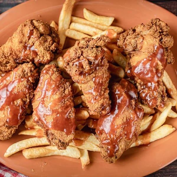 Crispy fried chicken pieces drizzled with barbecue sauce, served with golden french fries on an orange plate.