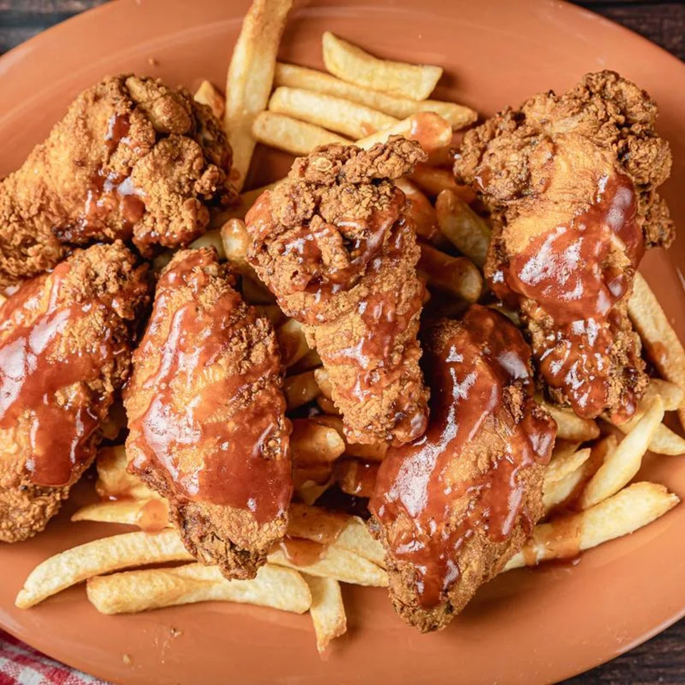 Crispy fried chicken pieces drizzled with barbecue sauce, served with golden french fries on an orange plate.