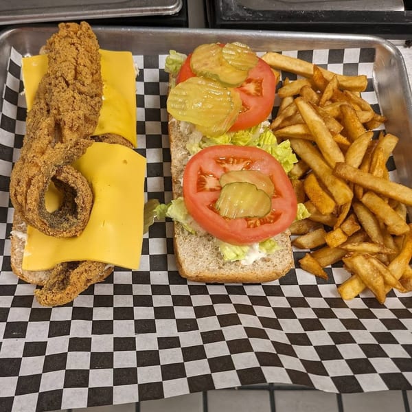 A Soul Goode fish sandwich with cheese, lettuce, tomato, pickles, and a side of fries.