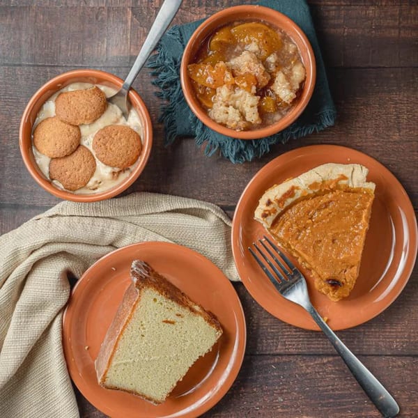 Soul Goode's banana pudding, peach cobbler, sweet potato pie, and pound cake on a wooden table.